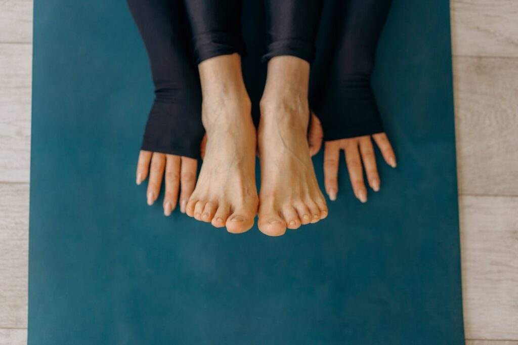Close-up of feet and hands on a blue yoga mat in a calm indoor setting.